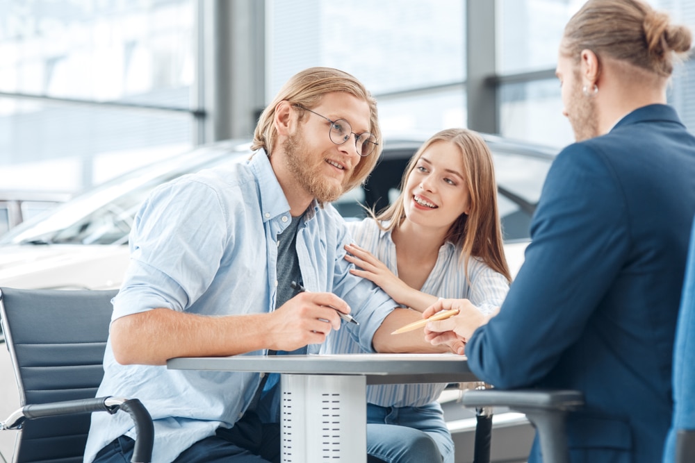 Young,Couple,Sitting,At,Table,Signing,Agreement,At,Salon,Buying qualities of a car salesperson